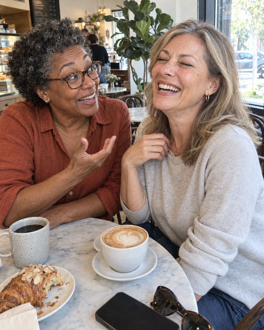 Two women in their 50s laughing over coffee
